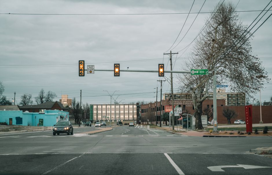 Mobilidade Urbana — View of a city street intersection with traffic and buildings under a cloudy sky.