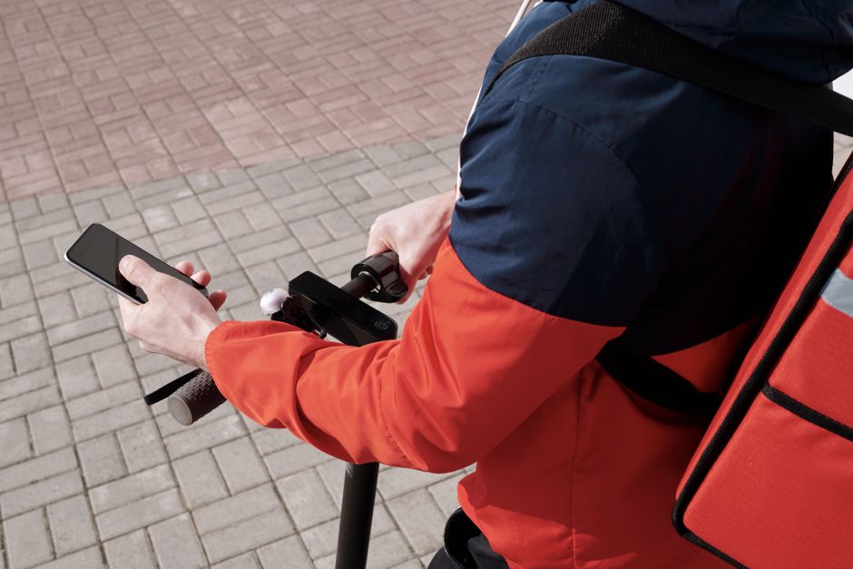 Mobilidade Urbana — A delivery person riding an electric scooter using a smartphone for navigation outdoors.